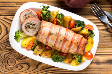 Pork roll wrapped in bacon stuffed with mushrooms and beans, vegetables on the side. Beautiful festive main dish for Christmas holidays