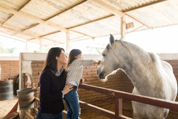 Woman With Daughter Touching Horse In Barn