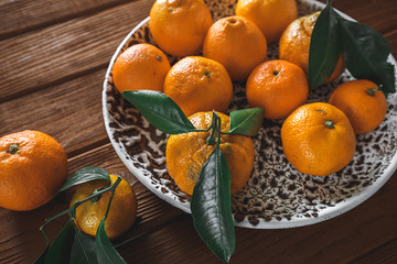 Fresh delicious mandarin oranges fruit or tangerines with green leaves in a bowl on wooden table