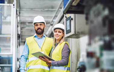 A portrait of an industrial man and woman engineer with tablet in a factory.