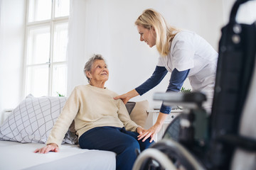 Obraz premium A health visitor talking to a senior woman sitting on bed at home.