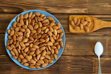 Nuts almond in a blue plate, spatula and spoonful of salt on a wooden surface. Healthy food