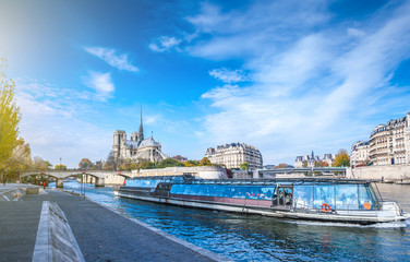 Fototapeta na wymiar Cathedral of Notre Dame de Paris at sunny autumn afternoon. Embankment of the Seine. Boat on scenic route. Tourists a walk and relax in warm weather. Blurred unrecognizable faces. Paris. France.