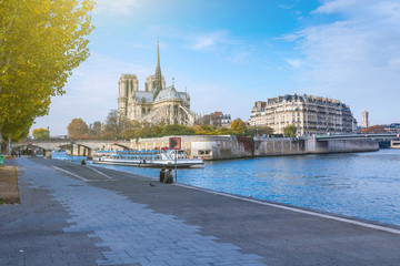 Obraz premium Cathedral of Notre Dame de Paris at sunny autumn afternoon. Embankment of the Seine. Boat on scenic route. Tourists a walk and relax in warm weather. Blurred unrecognizable faces. Paris. France.