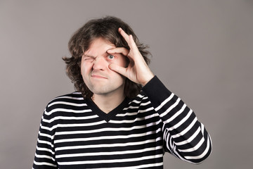 A man widen his eye with thumb and forefinger. Tired guy open his eye widely with fingers, having redness inside because of sleep deprivation, showing his problem to oculist on grey background