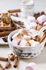 Ceramic cup of hot chocolate with marshmallow s'mores with homemade honey wafers and ingredients above over white marble table. Winter drink. Close up