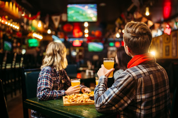 Fans watching match and drinks beer in sports bar - obrazy, fototapety, plakaty
