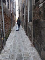 A tourist with luggage in a narrow street of Venice, Veneto, Italy.