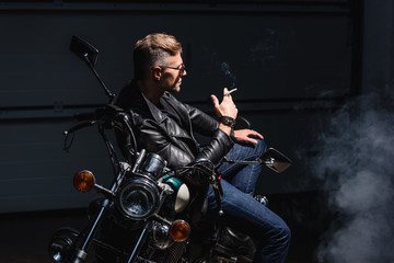 Fototapeta na wymiar handsome biker in sunglasses sitting on motorbike in garage