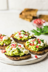 Avocado feta pomegranate toasts on cutting board. Selective focus, space for text.
