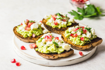 Avocado feta pomegranate toasts on cutting board. Selective focus, space for text.