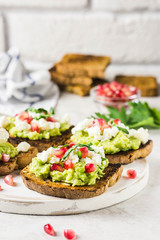 Avocado feta pomegranate toasts on cutting board. Selective focus, space for text.