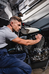 Fototapeta na wymiar handsome adult mechanic fixing motorcycle engine in garage