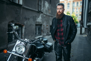 Fototapeta na wymiar Bearded biker in leather clothes against chopper