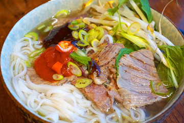 Vietnamese traditional food rice noodles with grilled pork spring onion, peanut, spring roll, lettuce, vegetable, carrot, Asian cuisine with chillies garlic fish sauce dipping sauce 