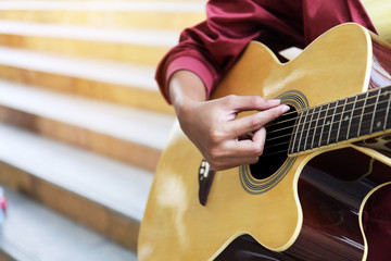 Close up beautiful woman playing acoustic guitar on walking street.