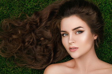 Beautiful woman with a healthy curly hair is lying on the grass