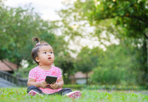Closeup little girl sit on grass floor and look at space of picture on park view background
