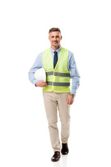Naklejka premium smiling engineer in safety vest holding helmet and looking at camera isolated on white
