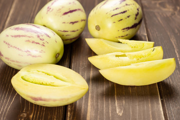 Set of three whole one half three slices of fresh striped pepino melon on brown wood