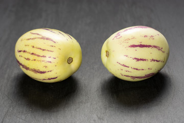 Group of two whole fresh striped pepino melon on grey stone