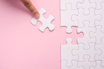 Close up of hand placing the last jigsaw puzzle piece on pink background. Business and team work...