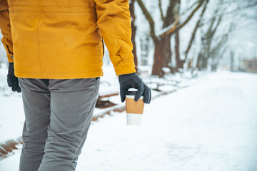 Fototapeta na wymiar man holding coffee cup walking by snowed city park body parts.