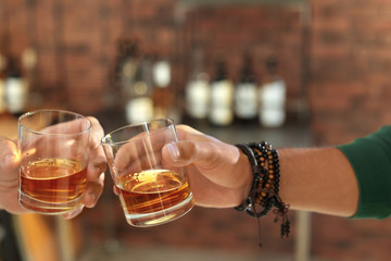 Friends toasting with glasses of whiskey indoors, closeup