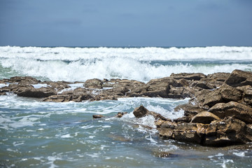 Fototapeta premium Waves crashing against a stones with foam and splashes. Ocean shore. Rocky beach
