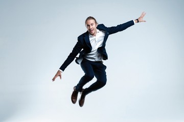 Young successful businessman in suit rejoicing, jumping over white background.