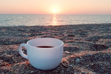 white cup on a sandy beach, against the sunset, rest, vacation, nostalgia.