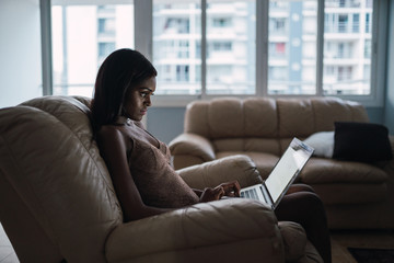 Fototapeta premium Modern black woman with laptop in armchair at home