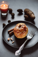 Baked apples in black plate with granola , nuts and cinnamon on gray table, with candle and bumps in the background