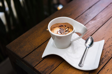 Beautiful cup of cappuccino coffee with plate on dark wooden table
