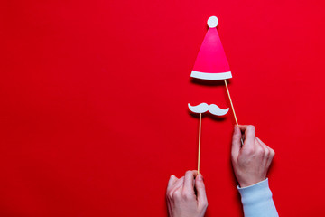 Hands holding Santa Claus Christmas photobooth props on a red background