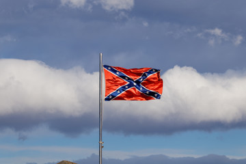 Confederate flag flutters on the wind against white clouds