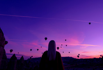 magische Morgendämmerung in Göreme Kappadokien Türkei. ein Mädchen in einer Schlucht in traditioneller Kleidung, umgeben von Luftballons in den Strahlen der aufgehenden Sonne