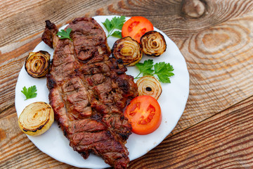 Grilled pork meat with onion, tomato and parsley in white plate on wooden table