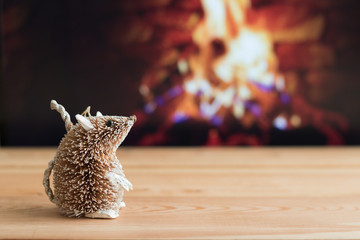 Decorative cute mouse is on a wooden table on a blurred background of burning fire in fireplace with copy space for your message. Concept: Christmas and New Year.