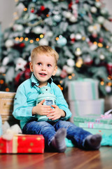 baby boy opens boxes with gifts under the Christmas tree and smiles