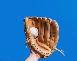 Hand in glove for a baseball game caught a leather white ball on a blue sky background. Sports...