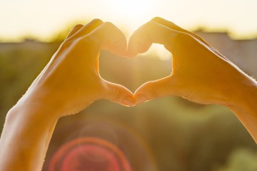Hands showing gesture heart, background evening sunset, city silhouette