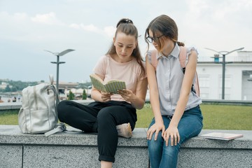 Outdoor portrait of two young beautiful girls students with backpacks, books. Girls talking,...