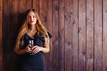 Fototapeta premium young attractive girl with a glass of champagne or wine on the background of the wall