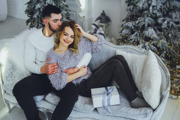 A couple in love gently smiling at each other, sitting on the sofa near the Christmas, New Year tree