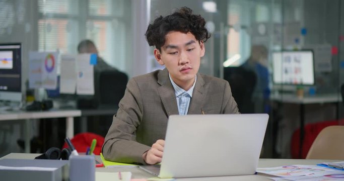 Tired asian young programmer putting off glasses