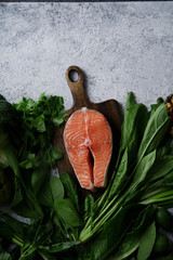 Fresh healthy food: vegetables, greens, fruits, walnuts and raw salmon steak on textured concrete background with copy space. Flatlay composition