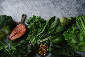Fresh healthy food: vegetables, greens, fruits, walnuts and raw salmon steak on textured concrete background with copy space. Flatlay composition