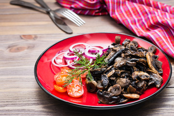 Ready-to-eat appetizer - fried mushrooms, cherry tomatoes and onions on a plate on a wooden table