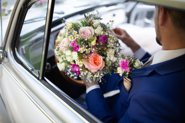 groom siting in a car with wedding bouquet